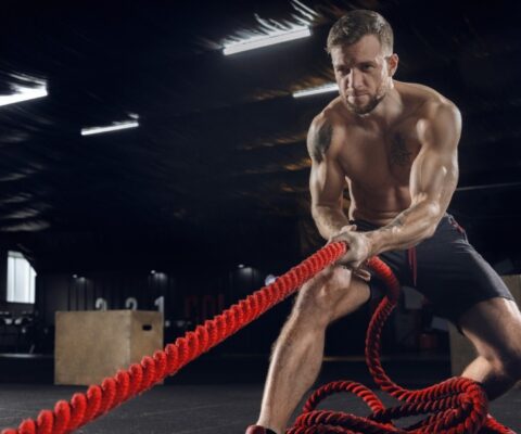 young healthy man, athlete doing exercise with the ropes in gym