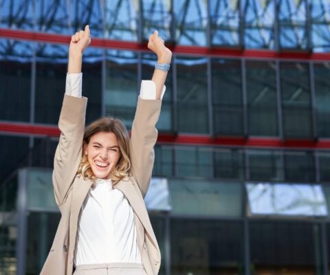 happy businesswoman dancing on street raising hands up